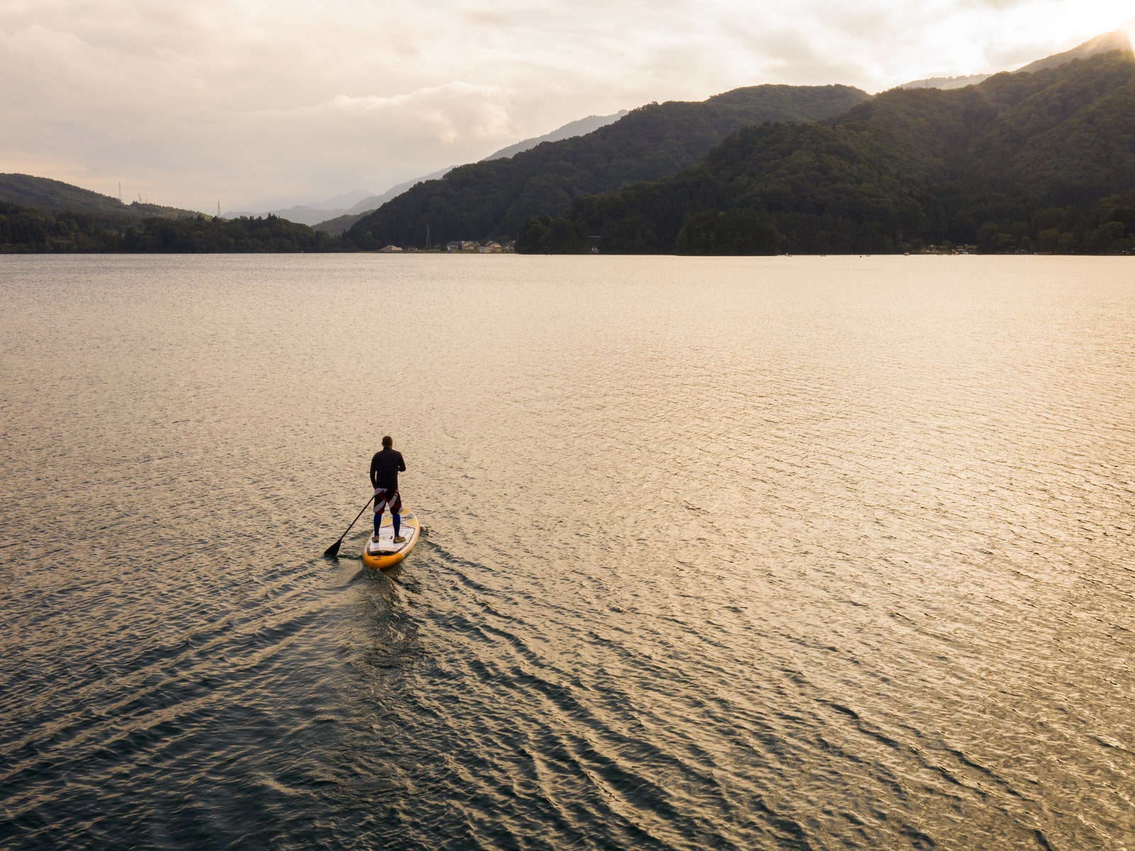 A man paddle boarding  alone in a large lake in the mountains during sunset